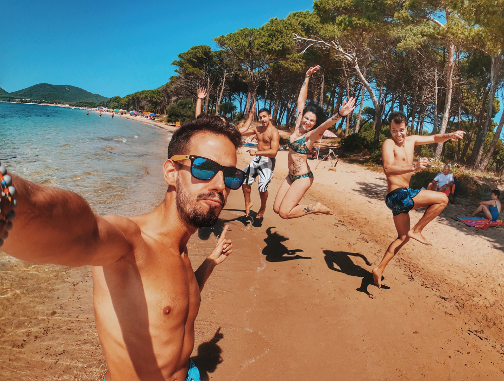 Friends jumping on sunny beach, taking selfie.