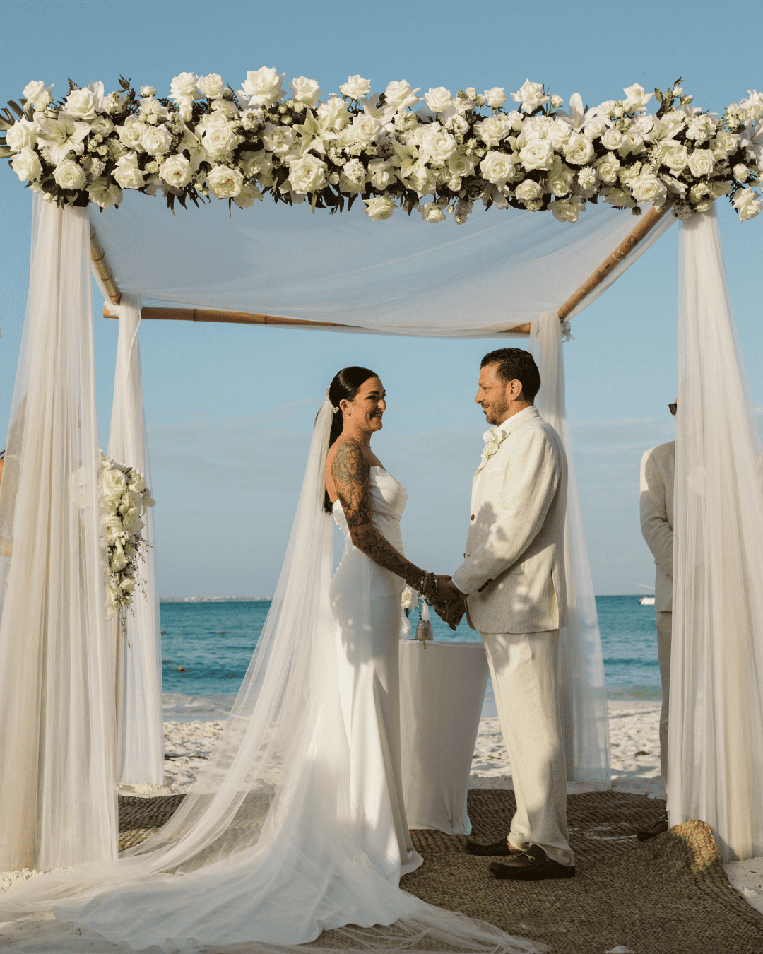 Couple holding hands under floral beach wedding arch.