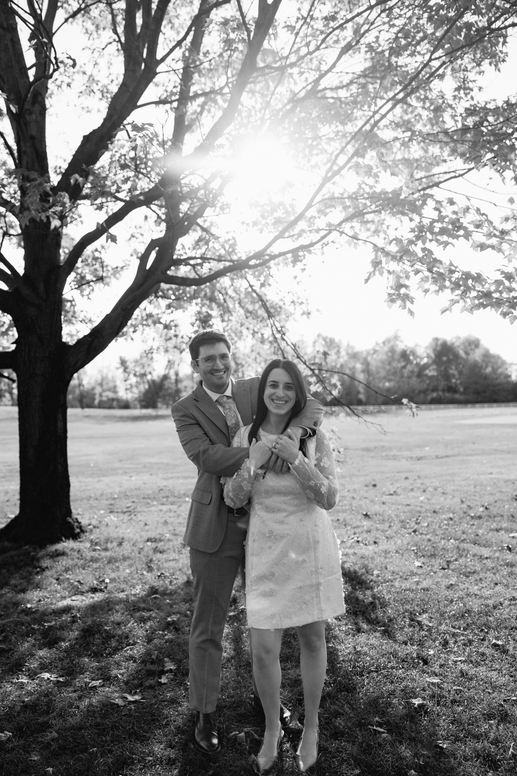 Couple smiling under tree in sunlit park