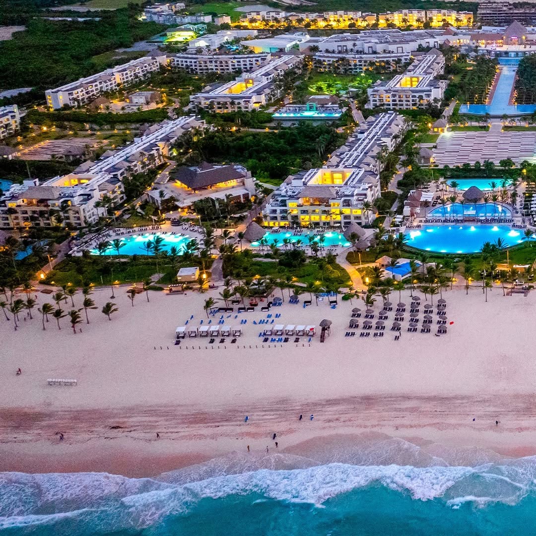 Aerial view of beachfront resort with pools and greenery.