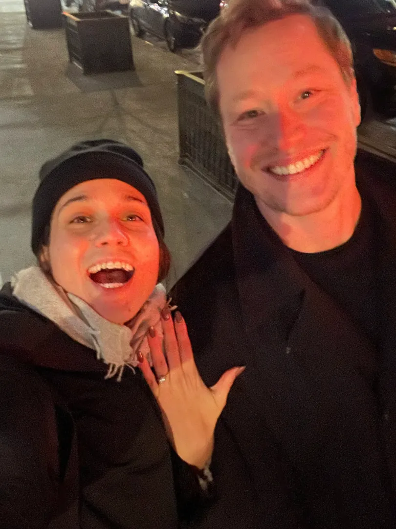 Two people smiling on a night street.