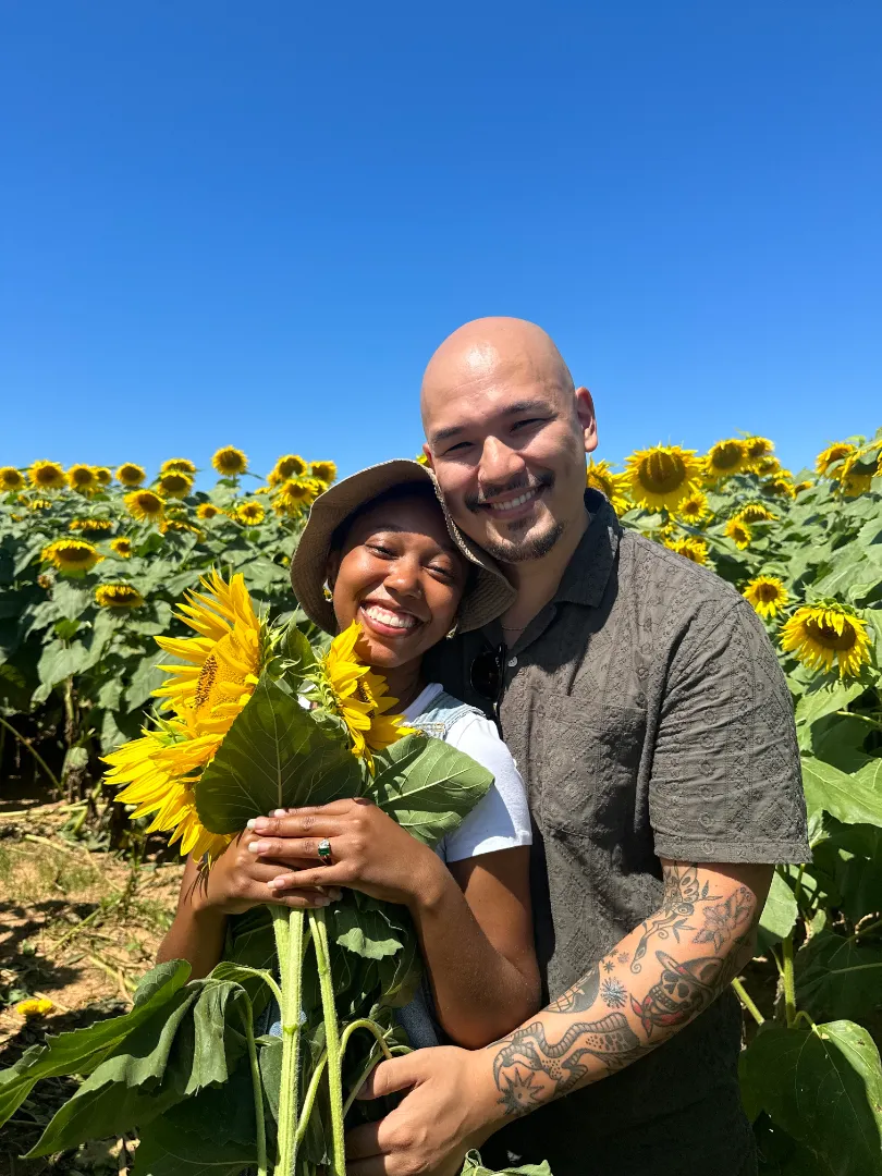 Couple smiling in sunflower field under clear sky.