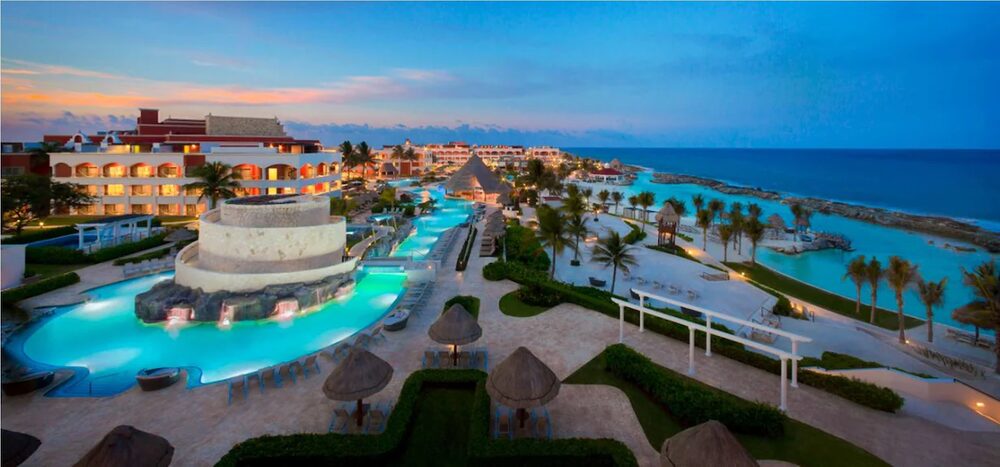 Aerial view of Hard Rock Hotel Riviera Maya at dusk, with the resort pools, palapas and the Caribbean beyond