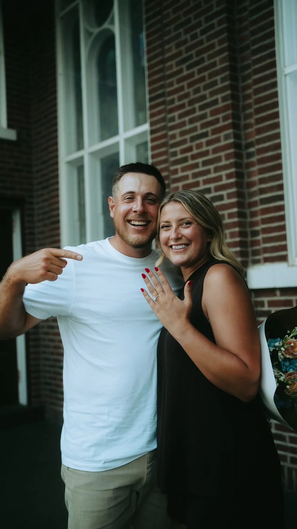 Nelius pointing to Kassidy's engagement ring outside a brick church